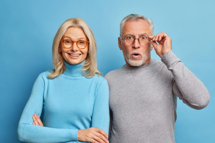 cheerful-middle-aged-woman-and-her-husband-pensioner-reacts-on-shocking-news-keeps-hand-on-spectacles-isolated-over-blue-wall.jpg