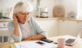 people-age-technology-and-finances-depressed-unhappy-retired-woman-paying-domestic-bills-online-trying-hard-to-make-both-ends-meet-sitting-at-kitchen-table-surrounded-with-papers-using-gadgets.jpg