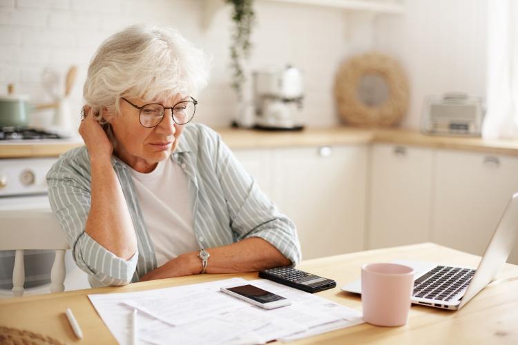 people-age-technology-and-finances-depressed-unhappy-retired-woman-paying-domestic-bills-online-trying-hard-to-make-both-ends-meet-sitting-at-kitchen-table-surrounded-with-papers-using-gadgets.jpg