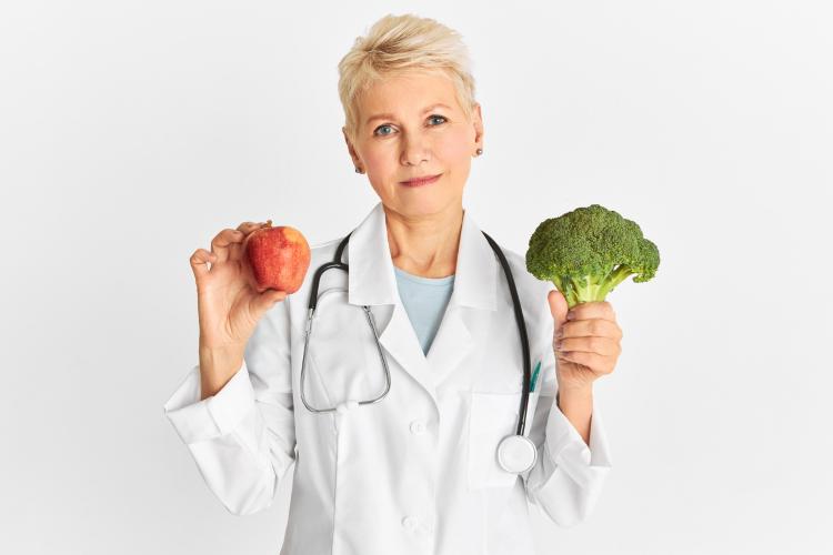 attractive-confident-mature-caucasian-female-doctor-holding-red-apple-and-green-broccoli-as-part-of-healthy-diet-to-reduce-risk-of-some-chronic-diseases-food-nutrition-and-health-concept.jpg