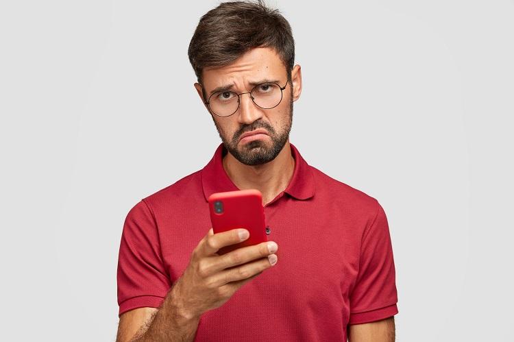 photo-of-displeased-young-unshaven-guy-holds-modern-red-smart-phone-being-unhappy-to-read-neagtive-news-in-internet-messages-with-friends-in-social-networks-connected-to-wireless-internet.jpg