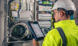 man-an-electrical-technician-working-in-a-switchboard-with-fuses-uses-a-tablet_169016-25055.jpg