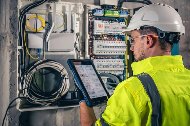 man-an-electrical-technician-working-in-a-switchboard-with-fuses-uses-a-tablet_169016-25055.jpg