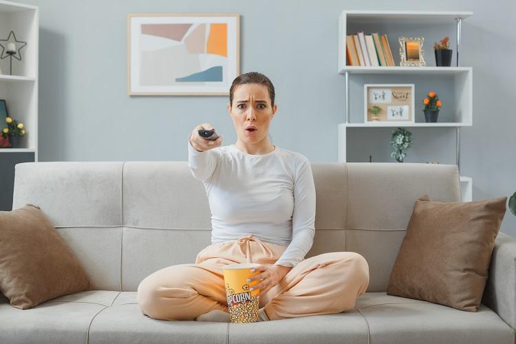 young-beautiful-woman-in-casual-clothing-sitting-on-a-couch-at-home-interior-holding-remote-watching-tv-with-bucket-of-popcorn-looking-at-camera-worried-and-confused-spending-time-at-home.jpg