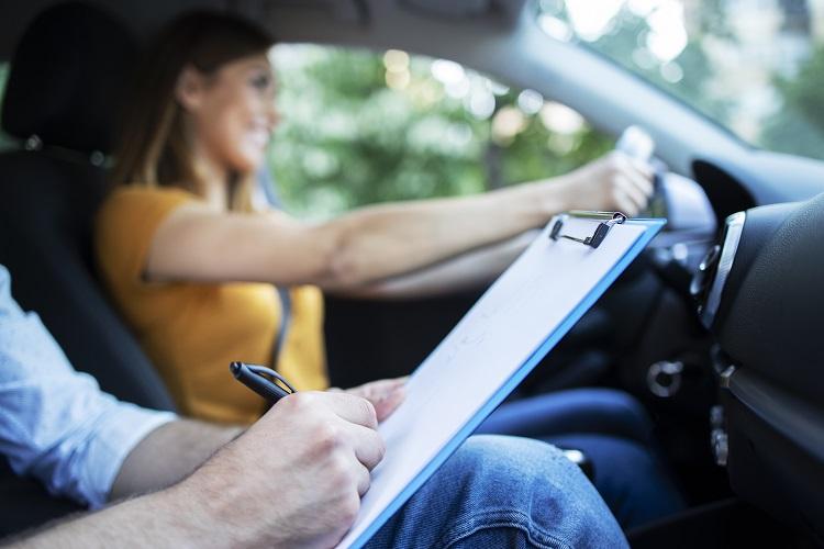 close-up-view-of-driving-instructor-holding-checklist-while-in-background-female-student-steering-and-driving-car.jpg