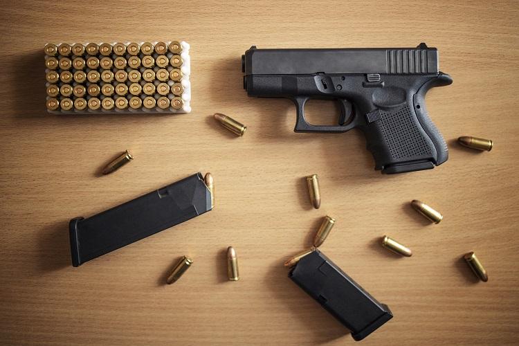 gun-with-box-of-ammunition-and-bullets-on-wooden-wall.jpg