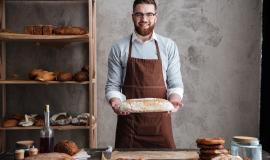 cheerful-young-man-baker-standing-at-bakery-holding-bread.jpg