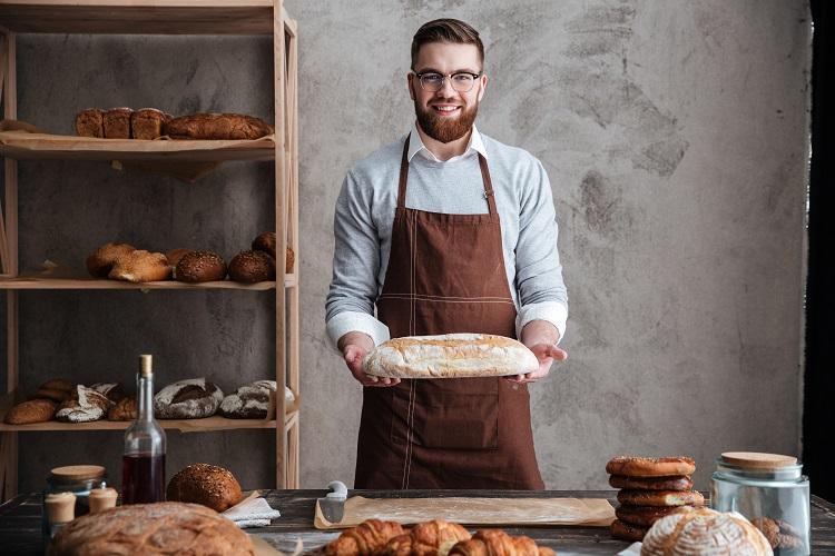 cheerful-young-man-baker-standing-at-bakery-holding-bread.jpg