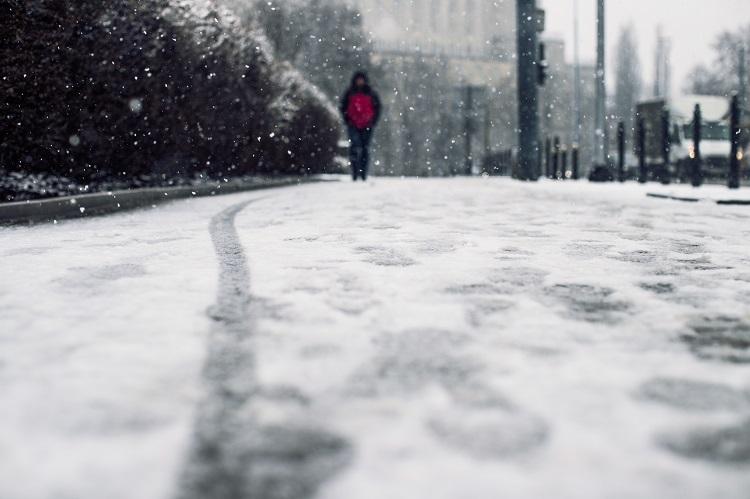 low-angle-shot-of-a-person-walking-on-the-snow-covered-sidewalk-under-the-snow.jpg