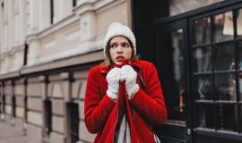 girl-in-snow-white-knitted-hat-and-mittens-is-shaking-from-cold-wrapping-herself-around-in-red-coat.jpg