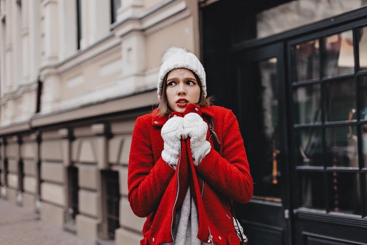 girl-in-snow-white-knitted-hat-and-mittens-is-shaking-from-cold-wrapping-herself-around-in-red-coat.jpg